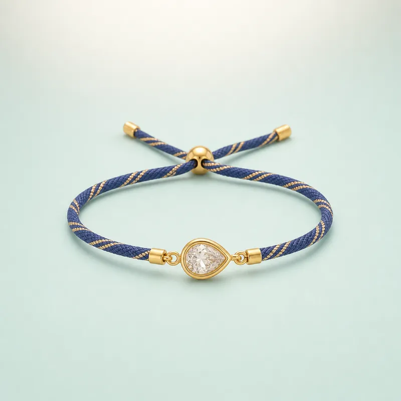 Gold pear-teardrop CZ solitaire rakhi · royal-blue cord  -  925 Sterling Silver on seaglass background