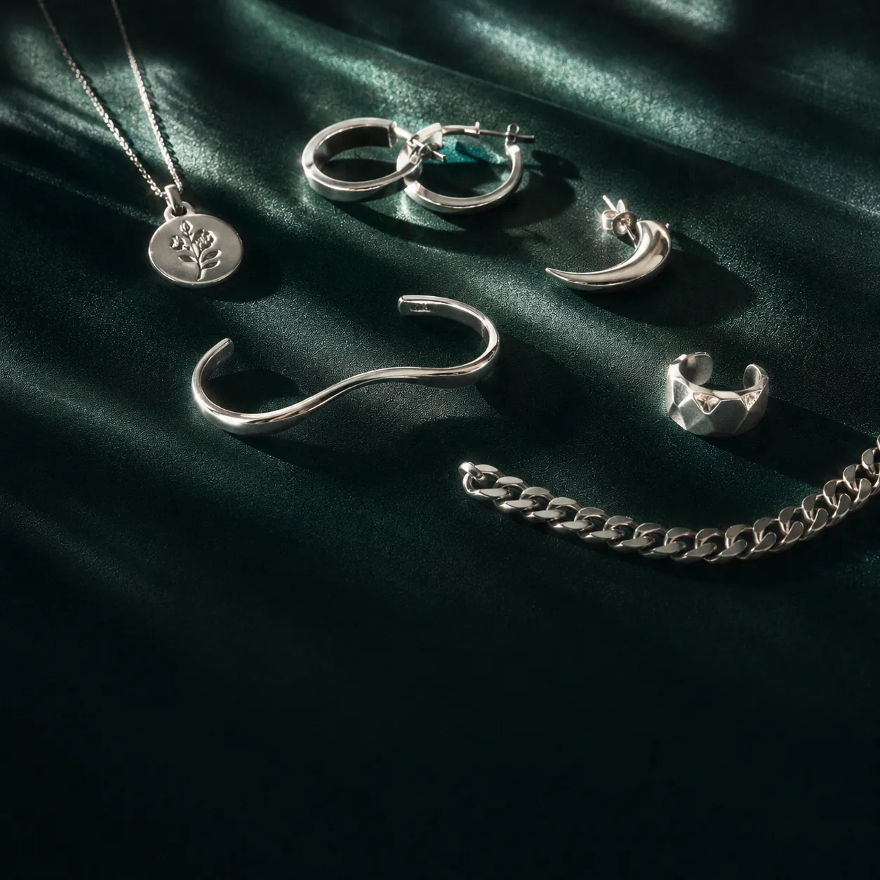 A refined flat-lay of five sterling silver pieces on layered ivory and deep emerald silk