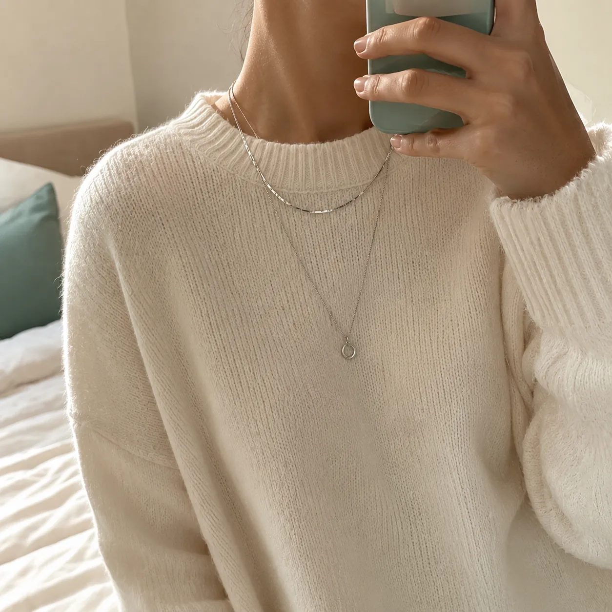 Layered fine silver chains over a cream knit sweater