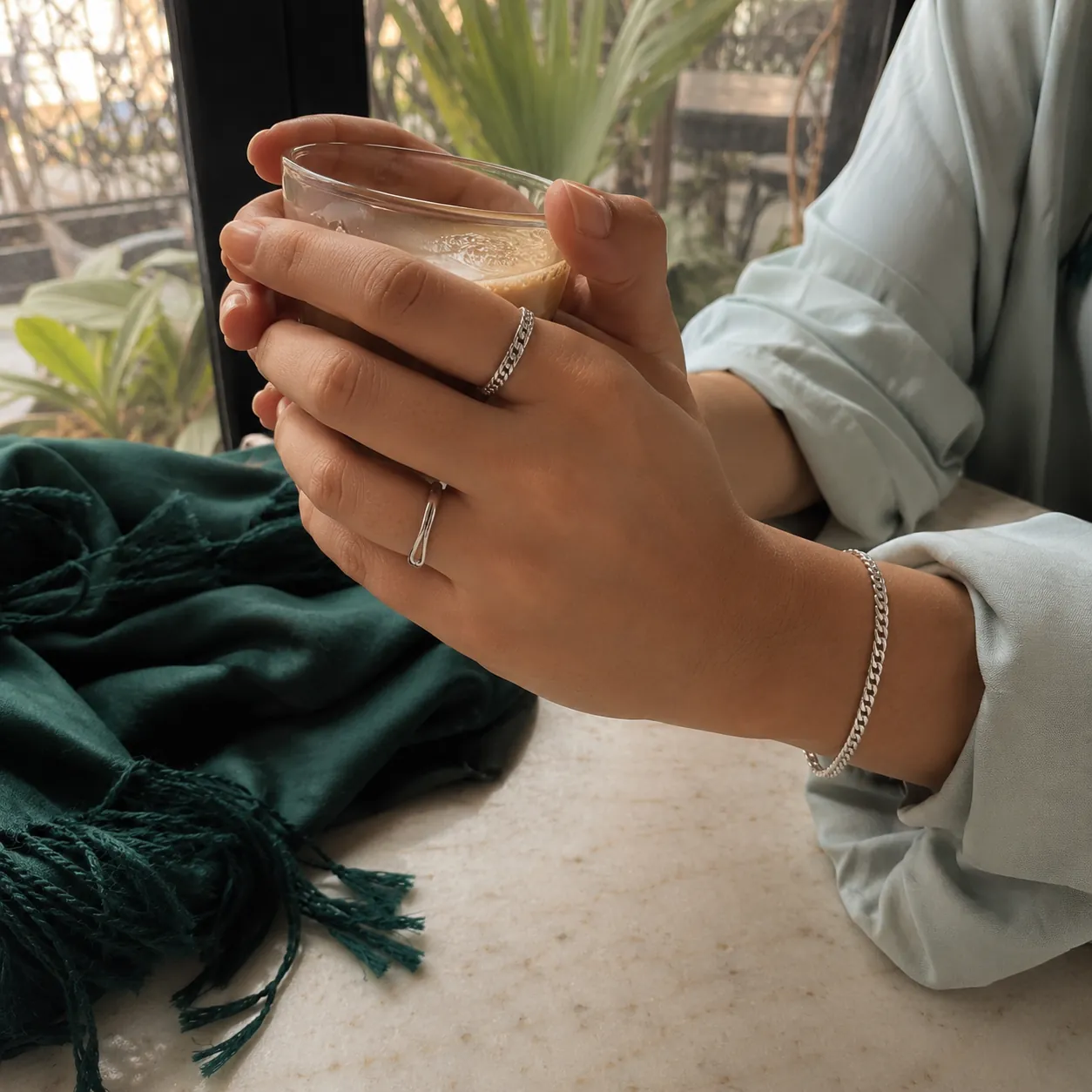 Hands cupping a chai glass, silver rings catching window light