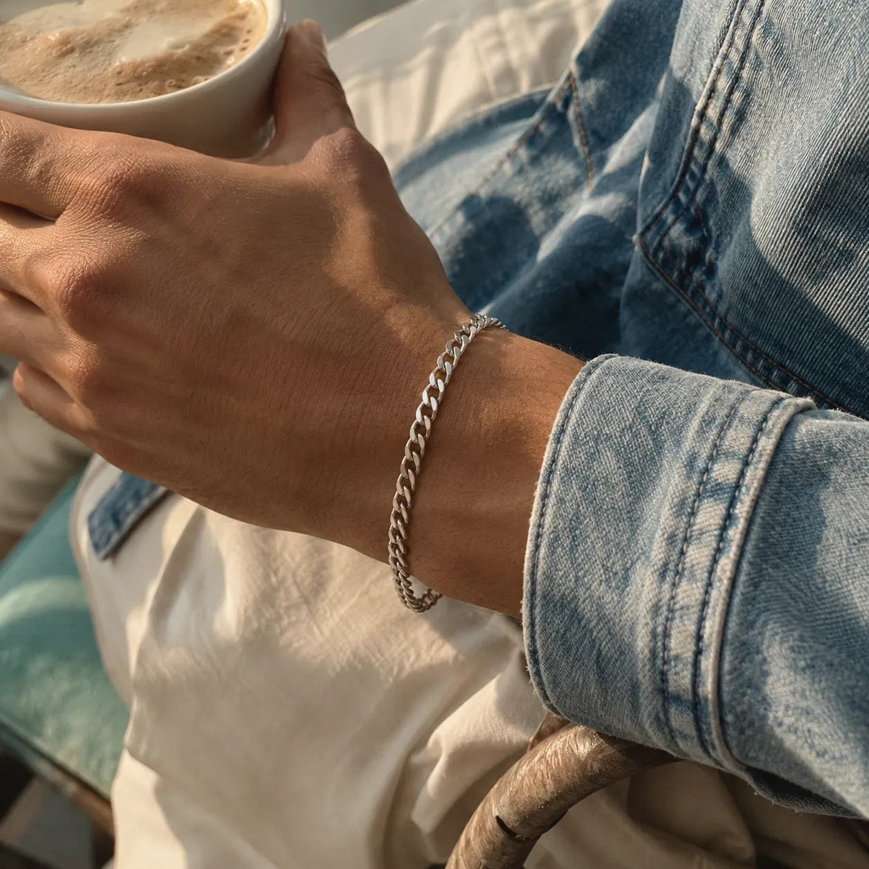 A man's wrist wearing a silver curb bracelet, holding coffee