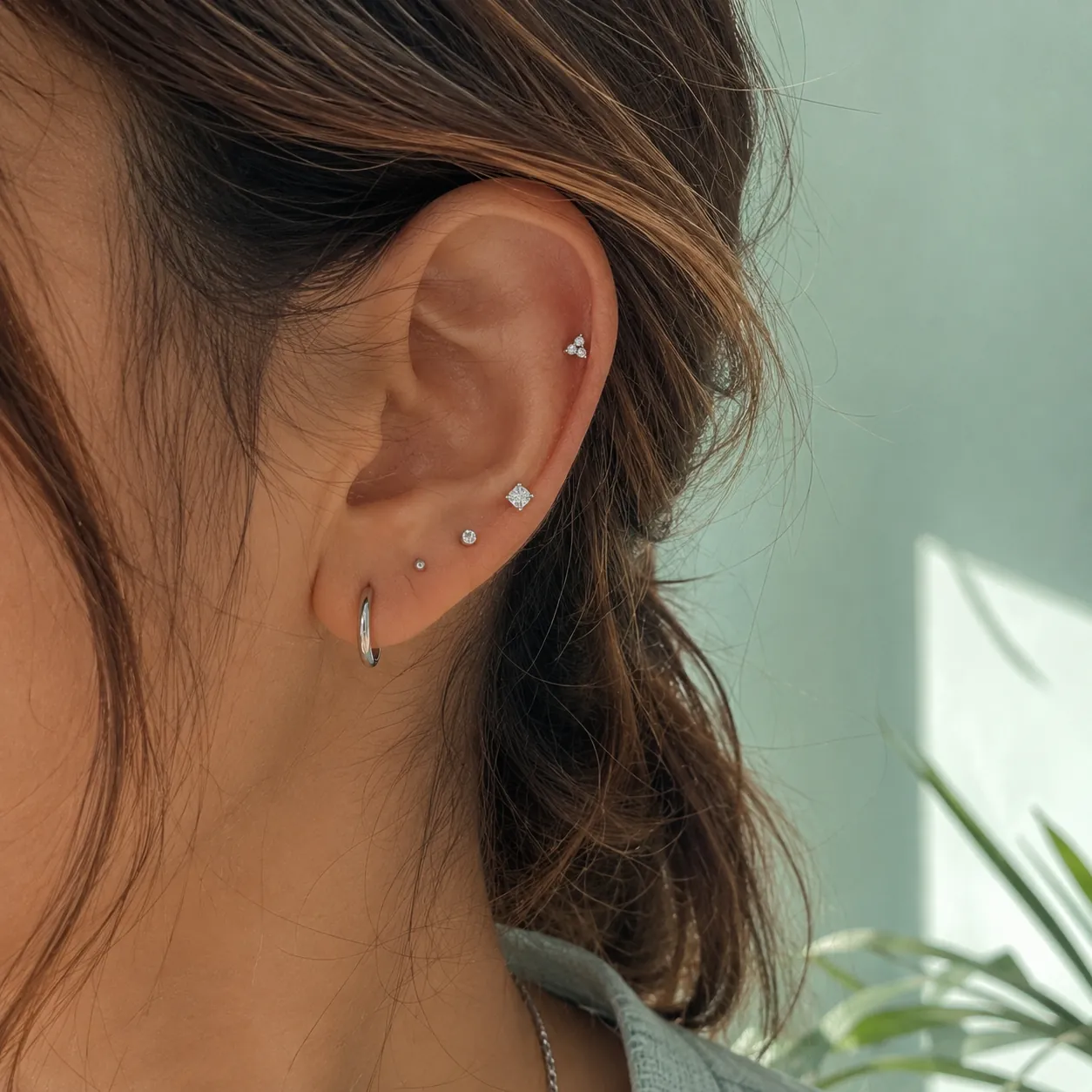 An ear with three tiny silver studs against a sea glass wall