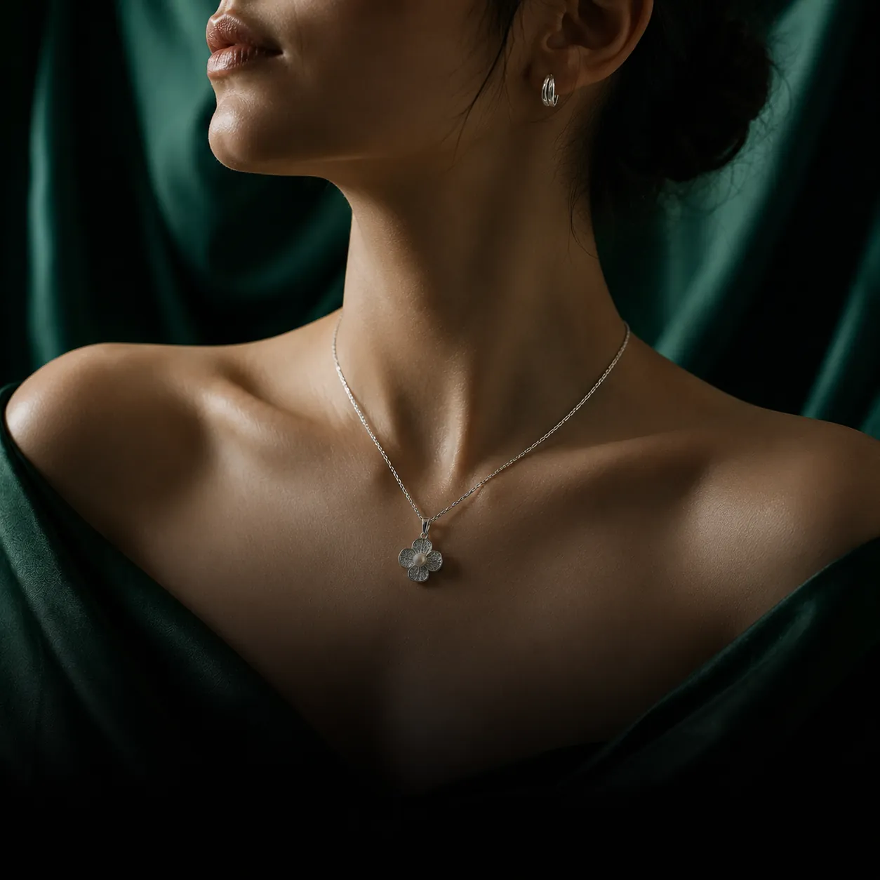 A statement silver drop pendant against emerald satin in warm evening light