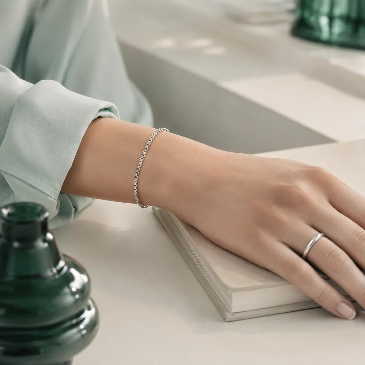 A slim silver chain bracelet and minimal ring resting on a pale desk