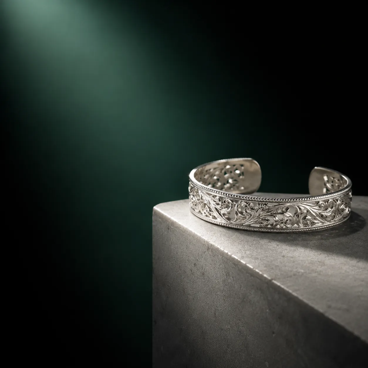An intricate handcrafted silver cuff on a stone plinth under gallery light