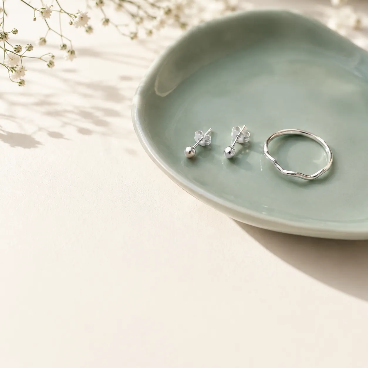 Tiny silver studs and a slim ring on a sea glass ceramic dish