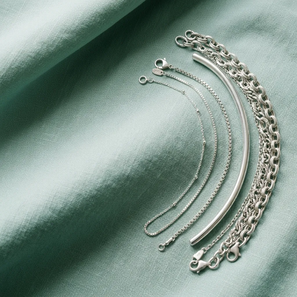 Silver chain bracelets and a polished cuff laid in flowing arcs on seaglass linen