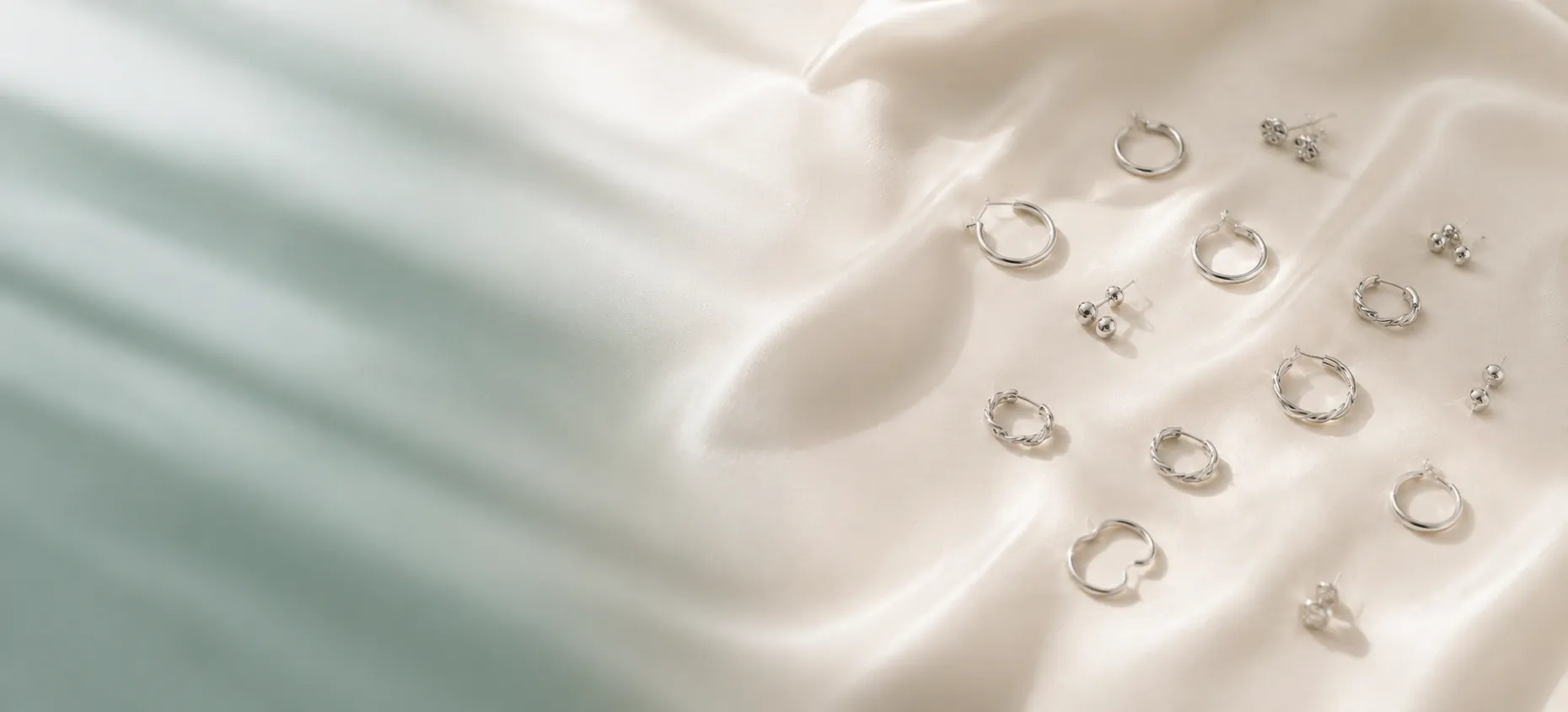 Silver stud and hoop earrings drifting across ivory silk
