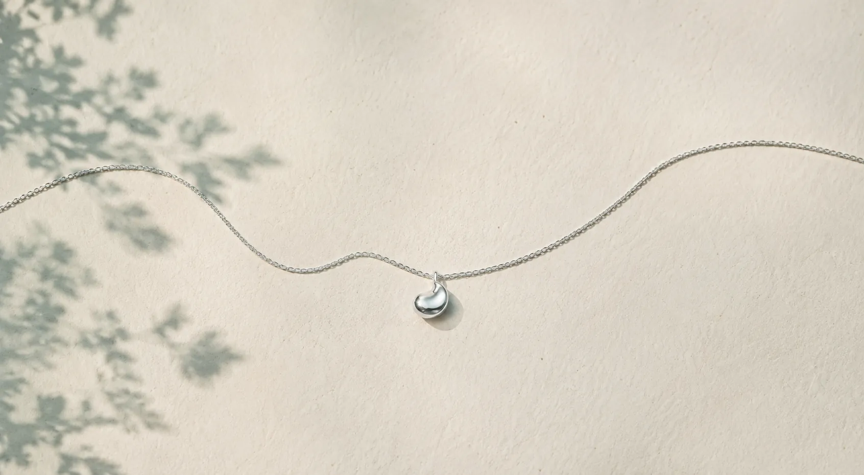 A fine silver chain and pendant draped across ivory handmade paper