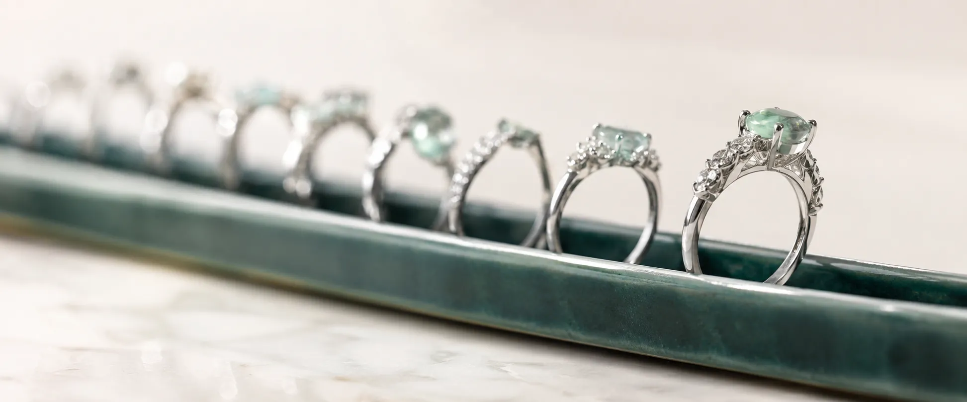 A row of sterling silver rings standing upright in an emerald ceramic channel